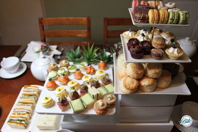 Tea service on white risers. Classic tea finger sandwiches. Open faced tea sandwiches, scones with jam and clotted cream, cupcakes, macaron, and tea breads